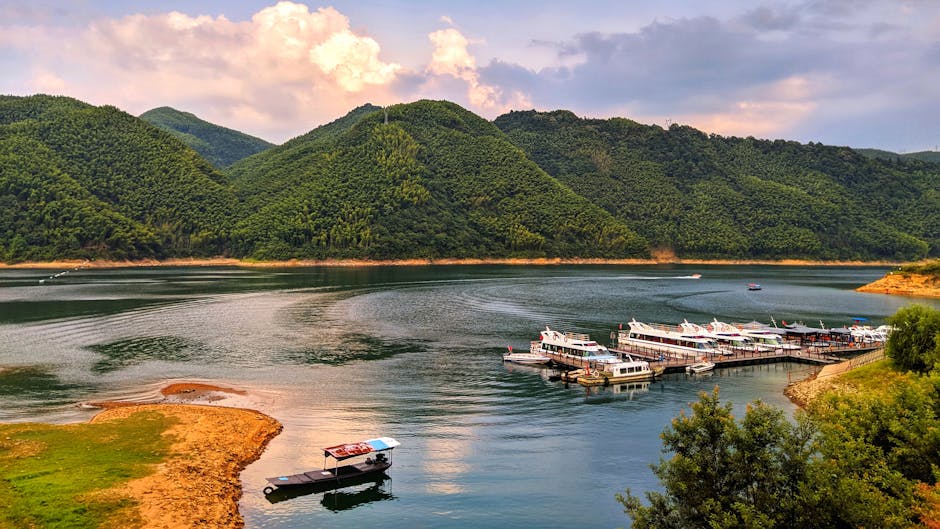 A tranquil lake scene with boats docked and lush green mountains in the background.